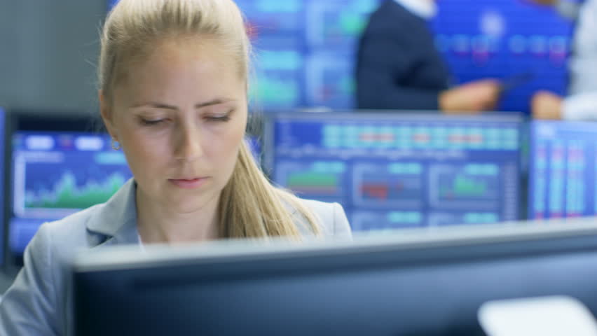 Experienced Stock Exchange Trader Making Sales and Buys at Her Workstation. Multi-Ethnic Team at Stock Exchange Office is Busy Selling and Buying Stocks on the Market. Displays Show Relevant Numbers.