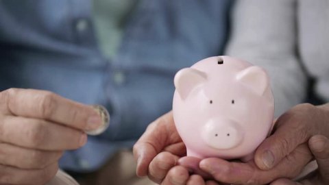 family, savings, old age and people concept - smiling senior couple putting money into piggy bank
