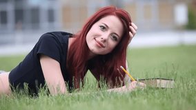 Redhead girl with notebook on green grass. Student concept
