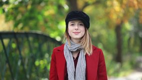 Video of young redhead woman in coat standing near bridge in park. Autumn time