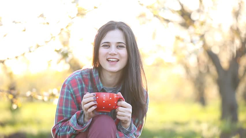 Brunet girl in shirt with cup of tea at apple tree garden. Spring time