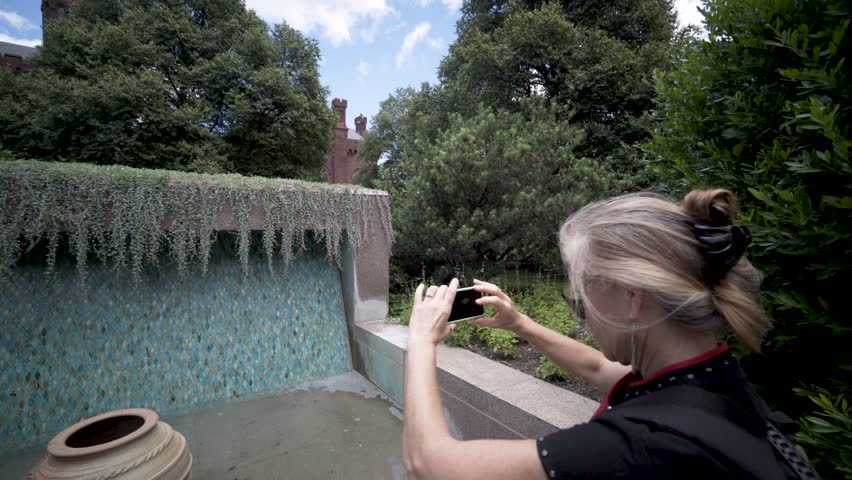 Pretty, mature woman taking a photo with her smart phone in the garden outside the Smithsonian Institution Castle and Arts and Industries buildings on the National Mall in Washington