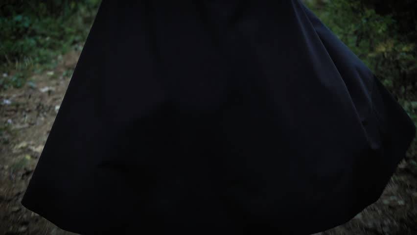 A woman in a long black cloak with a hood is walking along the park, the lady is walking with her back to us, we do not see her face Royalty-Free Stock Footage #32042698