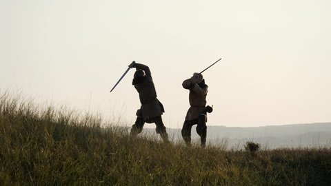 Silhouettes of two warriors Viking are fighting with swords. Contre-jour
