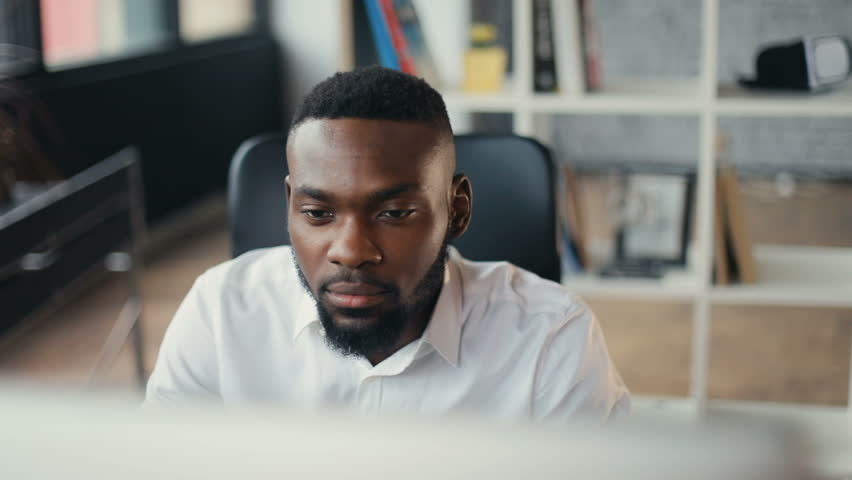 African American handsome male uses computer for work in modern office programmer serious looks at monitor screen freelance successful worker businessman solves engineering problems Slow motion Royalty-Free Stock Footage #32044096