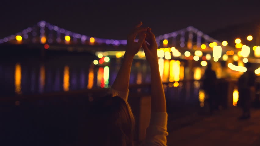 a young blonde girl with long curly hair dances in the night gown on the background of glowing fanfare. bright night illumination and a luminous bridge. The professional dancer moves quickly