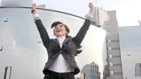 Happy caucasian business woman jumping and celebrating in front of office building. Win and success concept.