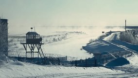 Guard post by barbed wire fence in Arctic Russia near winter road and river. Right-to-left pan shows snowy checkpoint, fog over water, and remote northern border landscape in cold conditions. - Powered by Shutterstock - Get 15% off with code: PIKWIZARD15