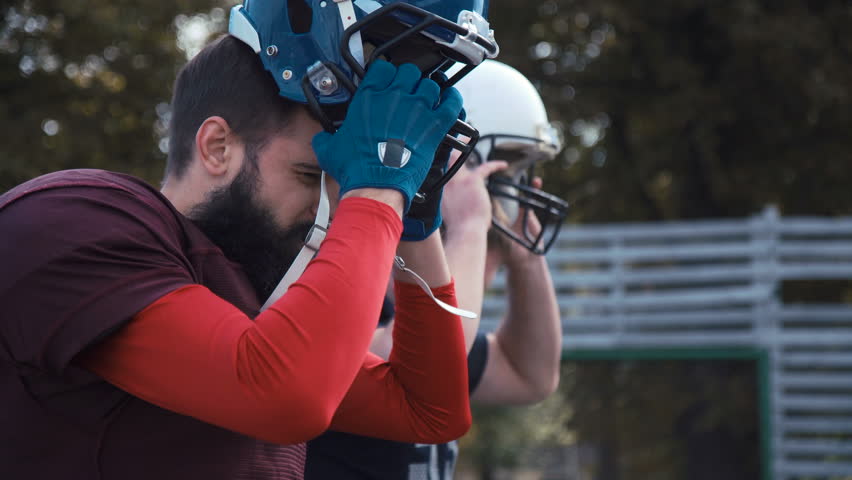 Side view of two American football players putting helmets on while preparing for game
