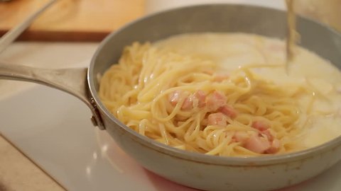 Closeup stirring with a shovel Italian pasta carbonara in a frying pan