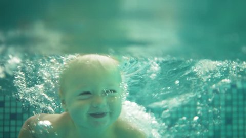 Happy smiling toddler is jumping and diving under the water in the swimming pool. An underwater shot. Slowmotion