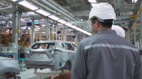 Automobile plant, modern production of cars, man and woman engineers discuss car production, assembly line of cars.
