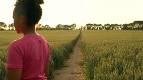 4K video clip of beautiful healthy mixed race African American girl teenager female young woman runner using smart watch and running on path through field of barley or wheat crops at sunset