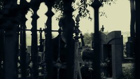 Woman with small boy in cemetery goes straight to camera. Mother and son in graveyard. Two figures in silhouette, central composition, horror horrified atmosphere and color stylization.
