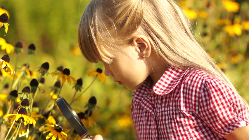 Girl looking at flower with a magnifying glass. Looking at camera
