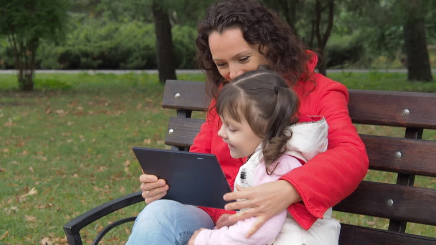Happy family with gadget in the park. Mother with a little daughter with a tablet on nature.