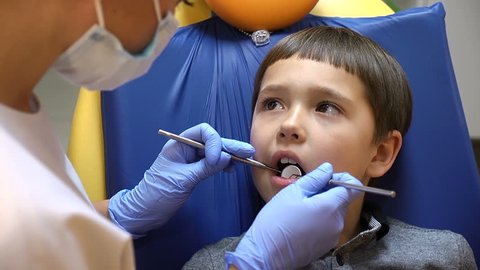 Health concept. A boy is in the dentist chair with his eyes full of tears getting dental treatment A female dentist in gloves holds medical tools.