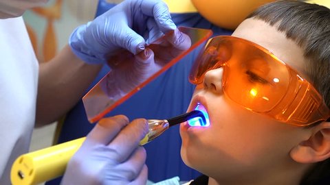Health concept. A boy at denyal clinic gets dental treatment to fill a cavity in a tooth. Dental restoration and material polymerization with UV light.