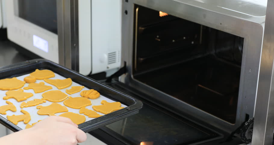 Young woman putting cookies into oven