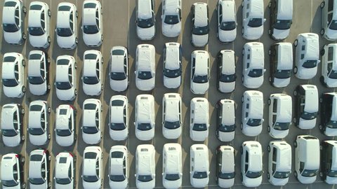 AERIAL TOP DOWN: Flying over big industrial zone with big parking lot of brand new cars. Many white cars waiting for sale and transportation at big sea port parking space. Heavy automobile industry.