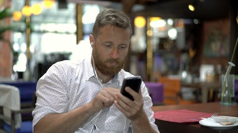 Man listening music and texting on smartphone in the restaurant, steadycam shot
