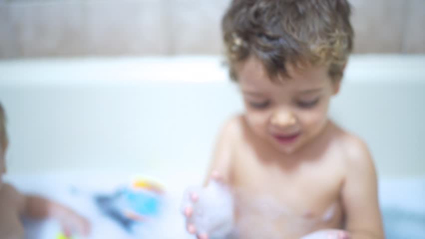 Happy little brothers playing together in the bath, A little baby and his brother playing together with the water and toys while taking a bath