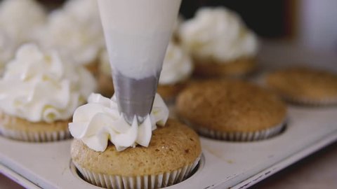 Decorating cup-cake with cream. Using cooking bag, confectioner making muffins for party. Shot of woman's hands putting butter cream on tasty cakes, home bakery concept