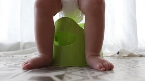 Baby sitting on chamberpot, Children's legs hanging down from a chamber-pot. Toddler gets up from the pot with a close-up only legs