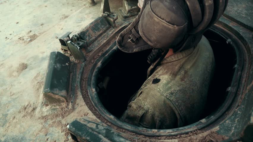 Tank man in military helmet sitting in tank while driving through battle field. Military man driving in war tank on shooting range