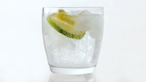Pouring sparkling water into a glass with ice, lemon and lime slices. White background.