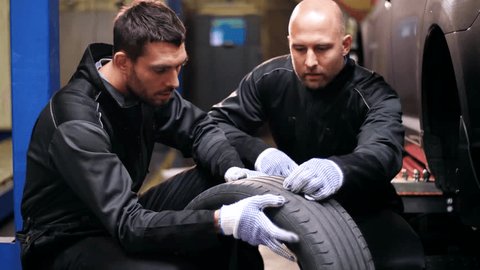 car service, repair, maintenance and people concept - two auto mechanics repairing wheel tire at workshop