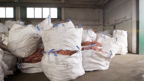 huge white bags with copper scrap from wires are lying in a warehouse of scrap metal processing plant