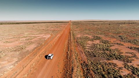 Drone shot vehicle traveling dusty road in Australian Outback.