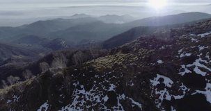 Forward aerial drone flight establisher over  forest woods with mountains and planes in winter. Snow in mountain nature outdoors.Sun flare.Travel exploring Alps. 4k establishing video