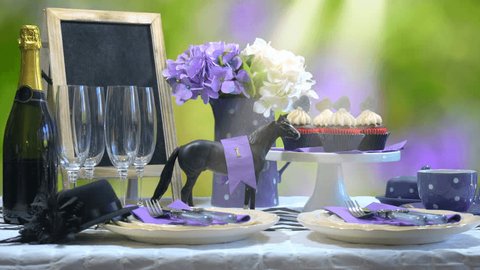 Horse Day Luncheon fine dining table setting with small black fascinator hat, decorations and champagne, wide static with lens flare.