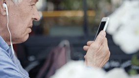 Closeup of senior man using headphones and holding smartphone while talking via video call