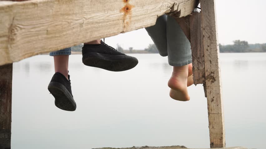 two girls relaxing by the lake sitting on the wooden pier swing with feet