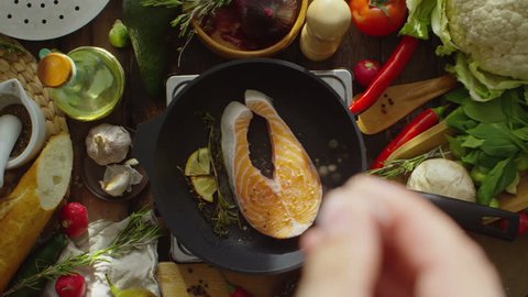 Cinemagraph of male hand adding seasonings to salmon steak frying on pan with lemon and herbs