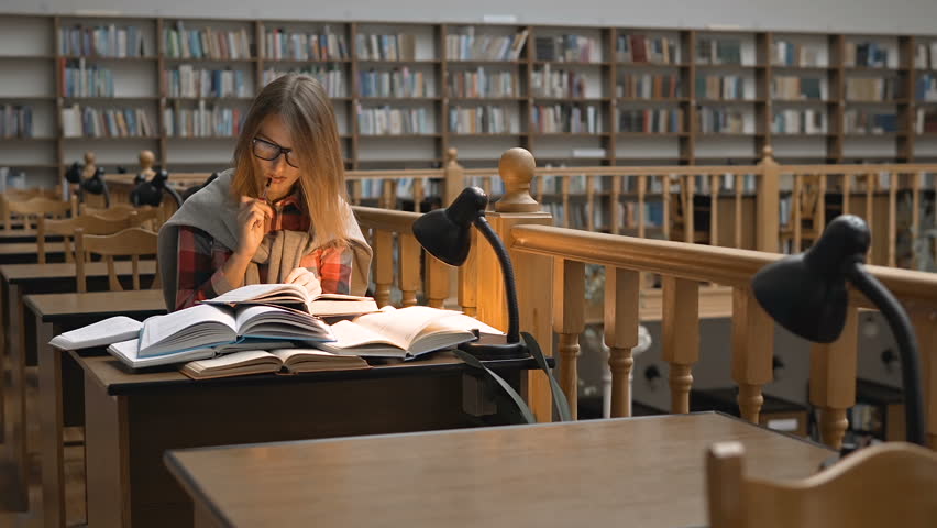 Pretty successful student wears glasses studying with books in the library Royalty-Free Stock Footage #32137243