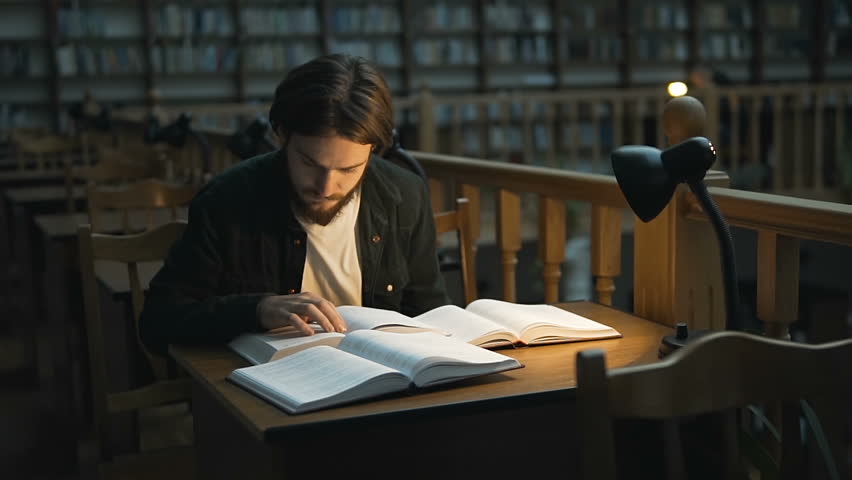 Young student reading in a library hall on table with lot of books and lamp, indoor dusk slowmotion Royalty-Free Stock Footage #32137324