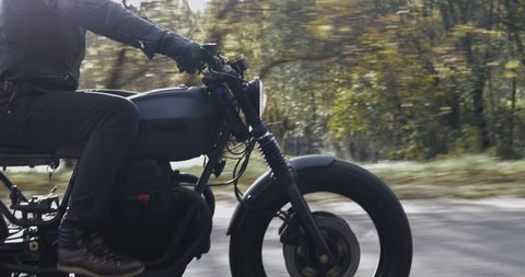 A guy in a black leather jacket and helmet riding a classic motorcycle on a forest road. Close-up on the side