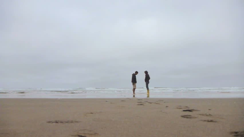 Man and woman walking from ocean on sandy, Oregon beach.