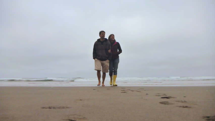 Man and woman walking from ocean on sandy, Oregon beach.