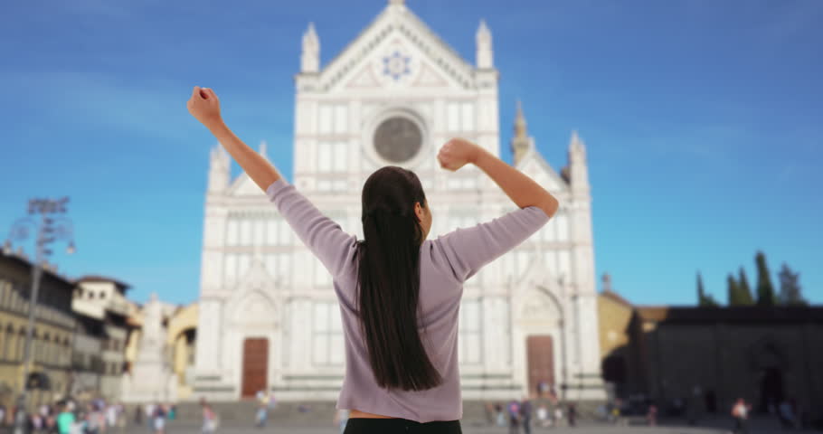Energetic brunette cheers in front of Basilica di Santa Croce in Florence. Happy Latina pumps her arms in excitement in front of Floretine basilica. 4k