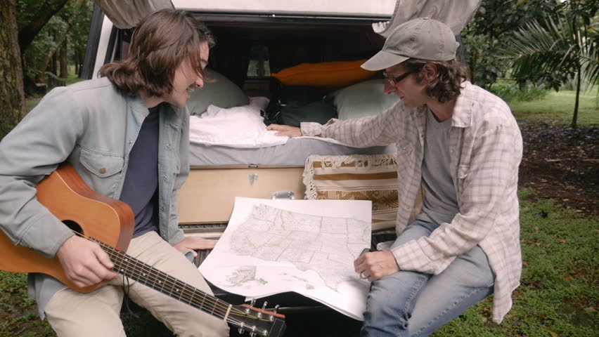 Two men trying to figure out where to go next on their road trip together while sitting with a map in slow motion Royalty-Free Stock Footage #32151349