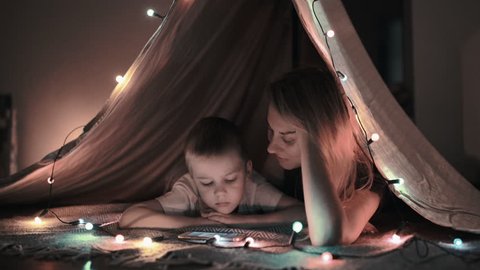 Mother and son play and watching smartphone in children's room in tent with Christmas decorations