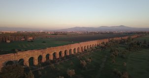 Video from above. Aerial view of the ancient Roman Aqueduct at sunset. Old ruins surrounded by a green public Park. Rome, Italy.