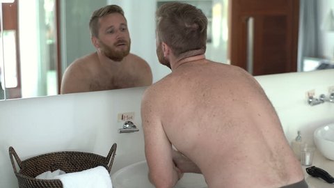 Handsome man washing his face and checking it in the mirror, steadycam shot
