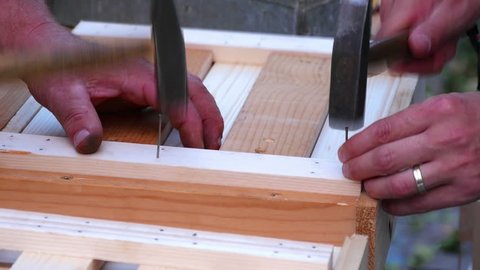 Two males hammering steel nails in to wood. Building a wooden box. Shot in slow-motion hd.