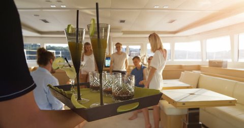 Following Shot of the Waiter Walking with a Tray Full of Exotic Cocktails, Serving them to a Company of Young People on a Yacht. Shot on RED Epic 4K UHD Camera.